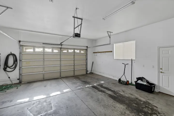 Spacious garage featuring a paneled overhead door with upper window inserts, an automatic opener, concrete flooring, a white interior door, and a horizontal window with blinds