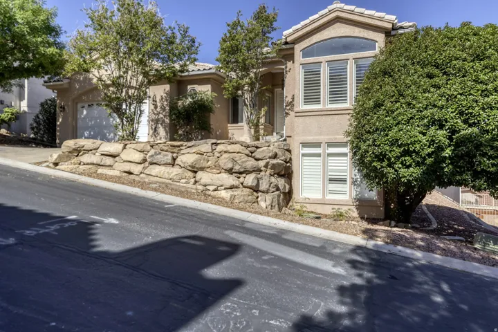 Stucco exterior residence featuring an attached garage, a stone retaining wall, and mature landscaping