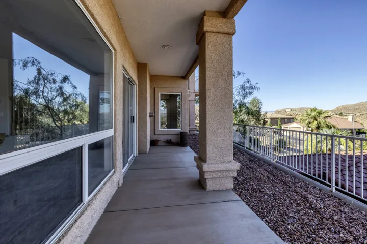 Covered concrete patio with stucco columns, metal railing, and a rock-filled landscape bed