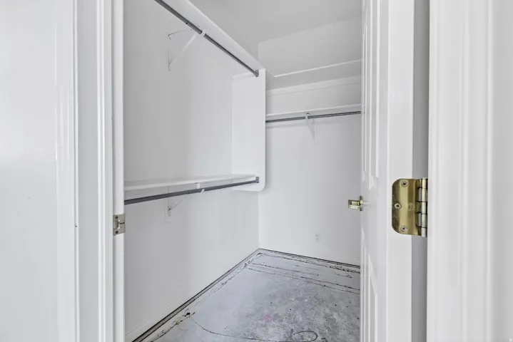 Walk-in closet featuring white walls, integrated shelving, and dual hanging rods