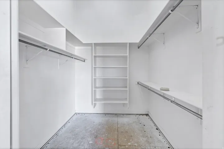 Walk-in closet featuring white painted walls, built-in shelving, and two clothing rods with integrated shelving