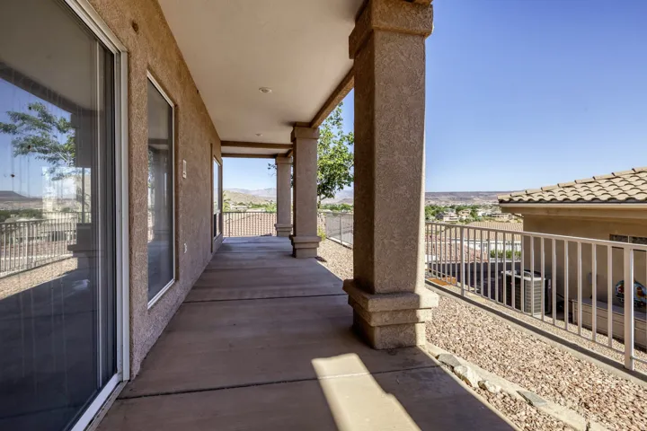 Expansive covered patio featuring a concrete surface, multiple large sliding glass doors, textured columns, a white metal railing, and a gravel-covered perimeter