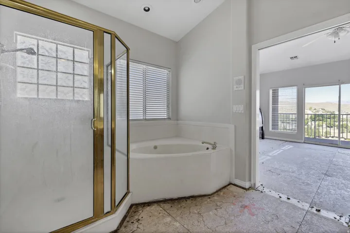 Bathroom featuring a corner soaking tub and an enclosed shower with gold-tone framing and frosted glass panels