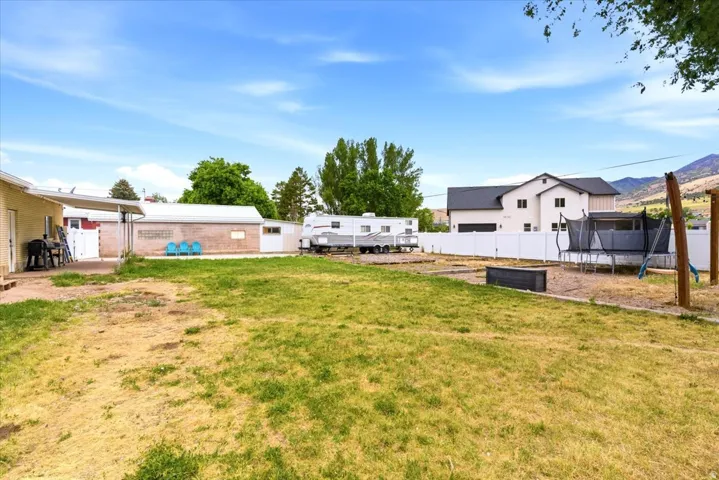 Spacious backyard featuring a large grassy area, a white privacy fence, and a brick outbuilding with an attached lean-to