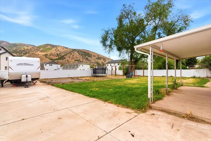 Expansive concrete driveway and patio area, featuring a carport with a white metal frame and soffit