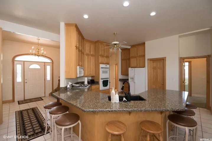 Kitchen with light wood cabinetry, a granite-look island with a built-in sink, and white appliances