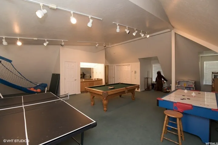 Spacious recreation room featuring track lighting, sloped ceilings, and green carpeting