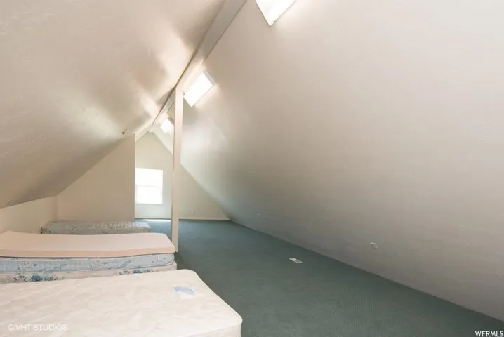 Attic space featuring sloped ceilings, recessed skylights, and light green carpeting