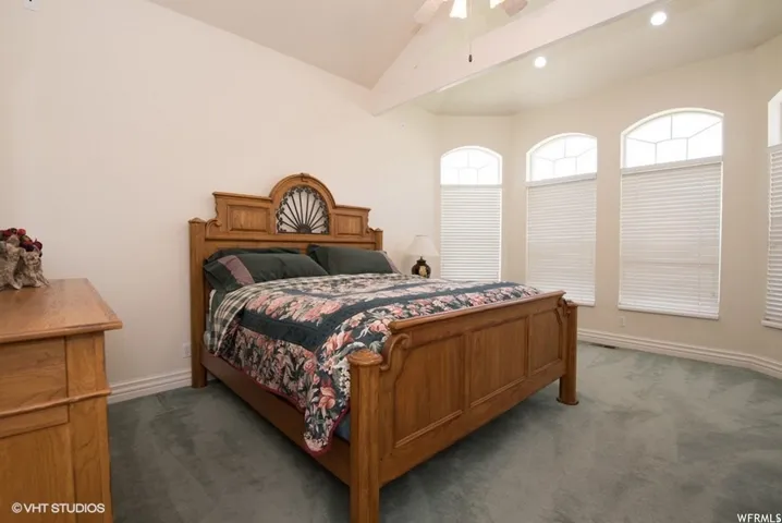 Bedroom featuring vaulted ceilings with exposed beams, three arched windows, recessed lighting, and soft green carpeting
