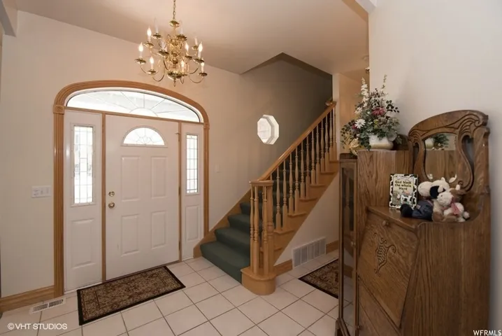 Entryway featuring a white paneled door with sidelights and an arched transom, a brass chandelier, a wood-finish staircase with balusters, and square tile flooring