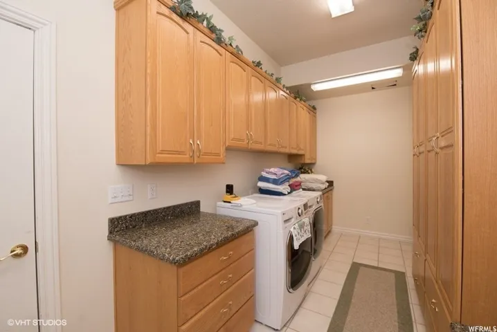 Laundry room featuring extensive wood cabinetry, granite-finish countertops, and durable tile flooring