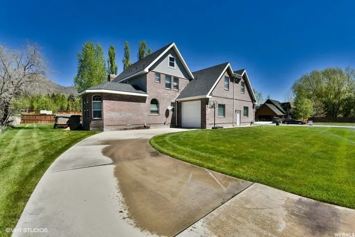 Brick exterior with a gabled roofline, featuring an attached garage with a white door, a paved driveway, and expansive green lawns