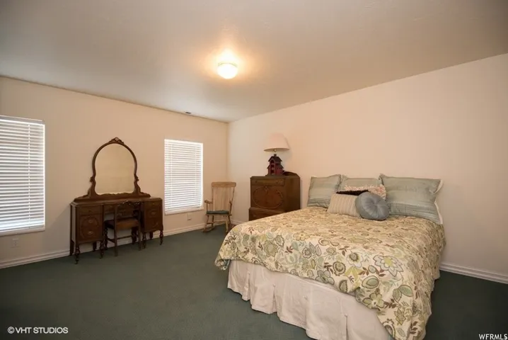 Spacious room featuring neutral painted walls, two windows with horizontal blinds, and deep green carpet flooring