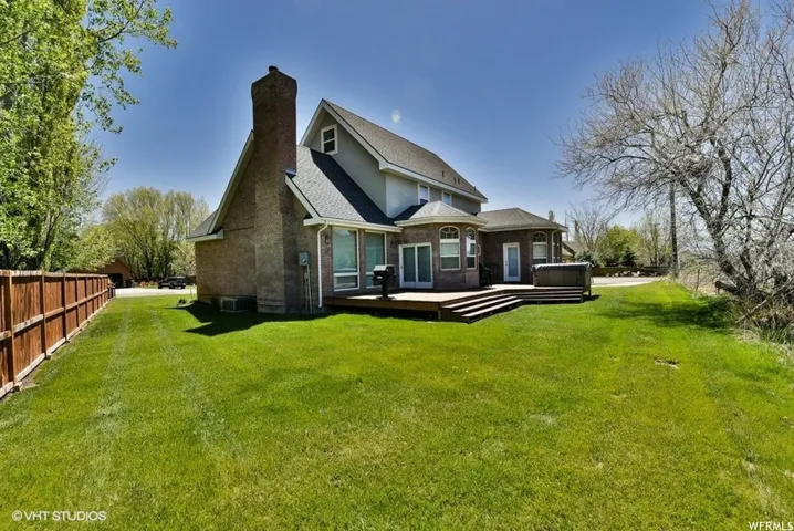 Rear exterior featuring a multi-level wood deck, an attached spa, and a spacious green lawn