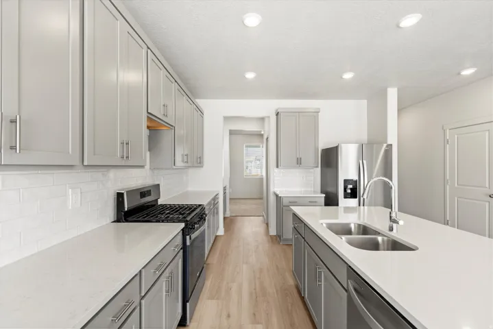 **DISLCAIMER** Interior package may vary. Modern kitchen featuring light gray cabinetry, stainless steel appliances, a double basin sink, light wood-finish flooring, and recessed lighting
