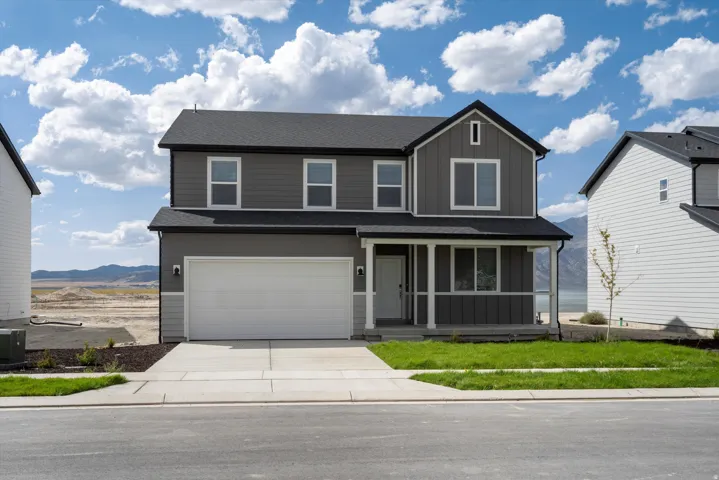 Two-story contemporary residence featuring a dark gray and light gray facade, attached two-car garage, covered porch, and a landscaped front yard with a concrete driveway