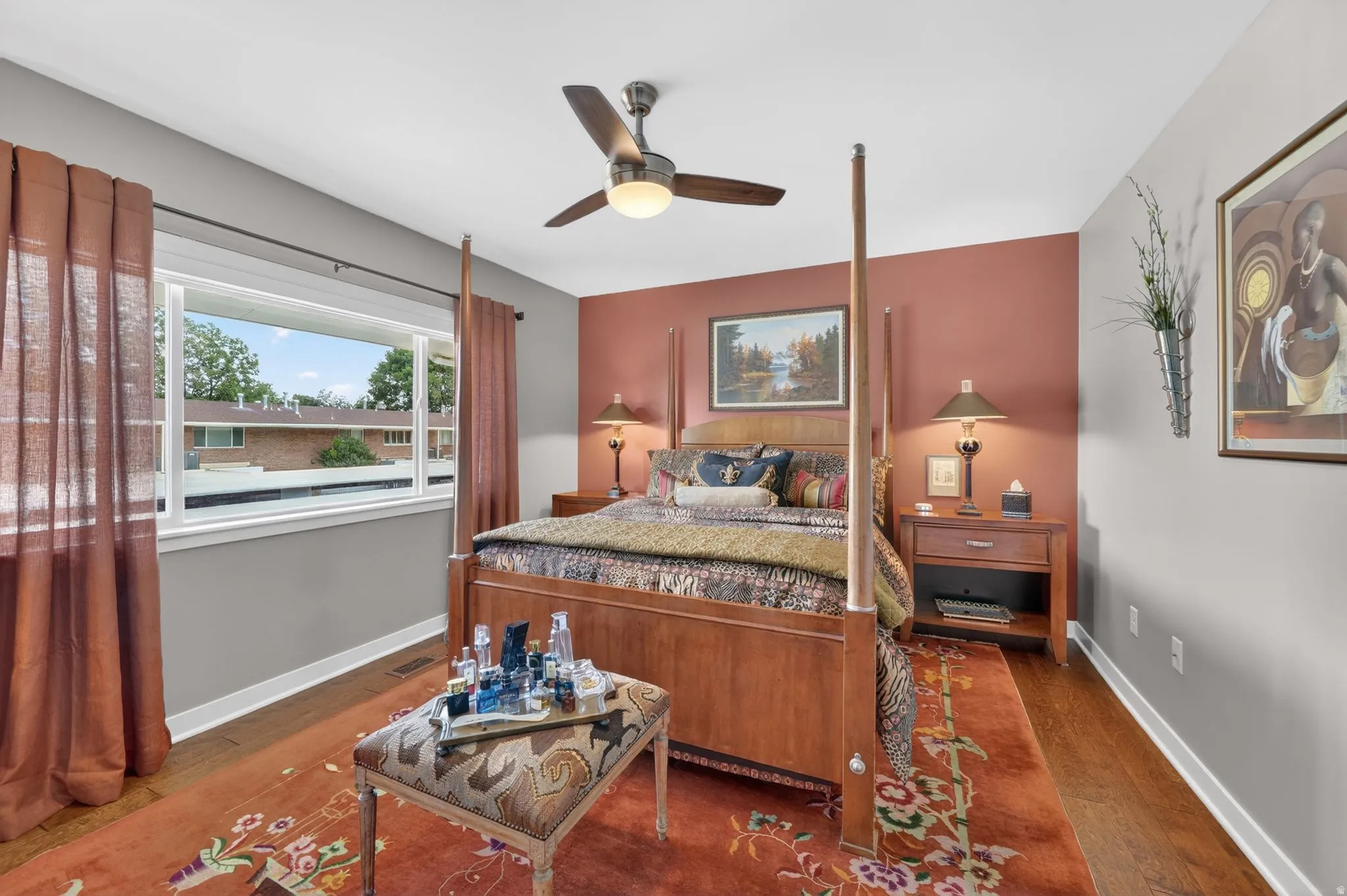 Spacious room featuring engineered hardwood flooring, a ceiling fan with integrated lighting, a large window, and an accent wall