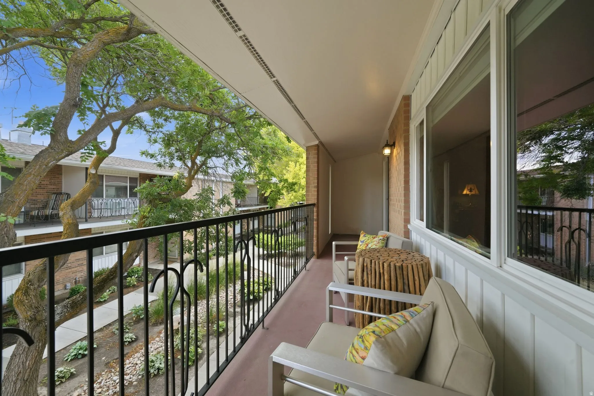 Spacious covered balcony featuring a black wrought-iron railing, white trim, and an exterior wall sconce
