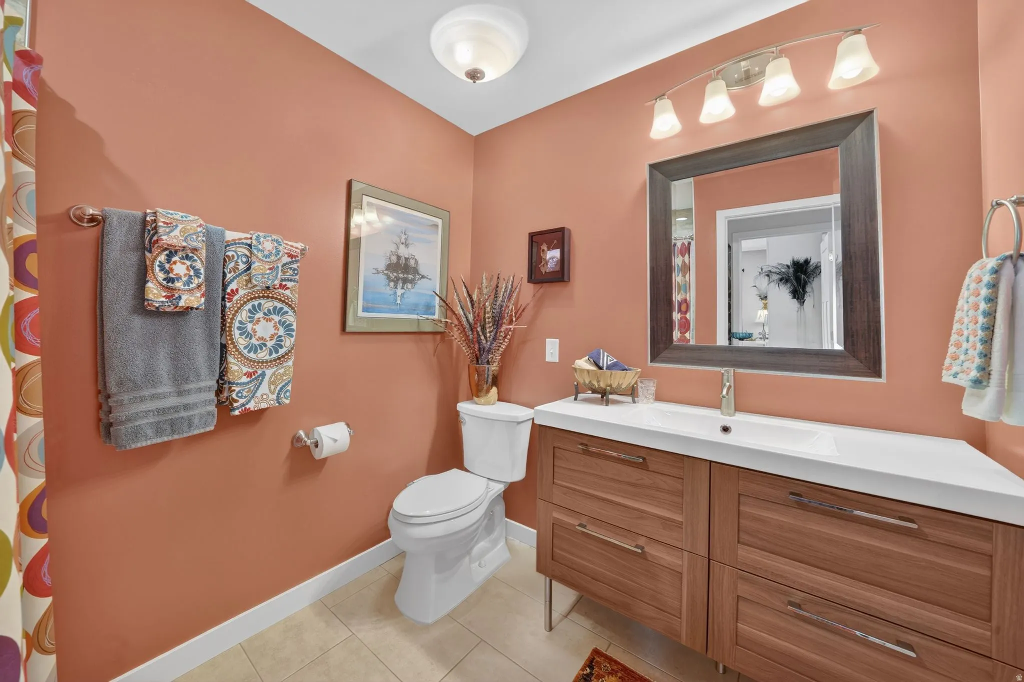 Guest bathroom featuring a wood-finish vanity with drawer storage, a white integrated sink, a framed mirror, and a four-light vanity fixture as well as a spacious tiles walk-in shower with recessed niche