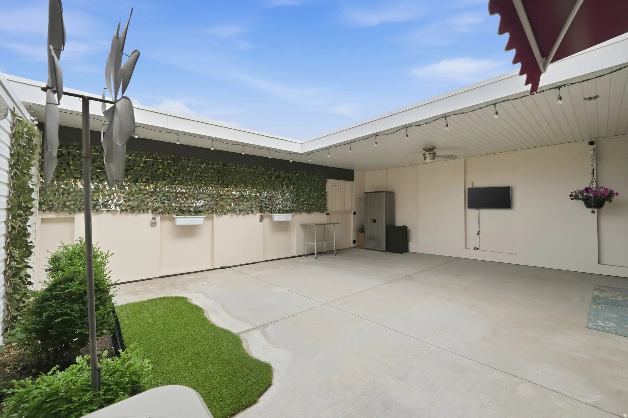 Spacious outdoor patio area featuring a concrete surface, overhead string lighting, a ceiling fan, and an artificial turf accent