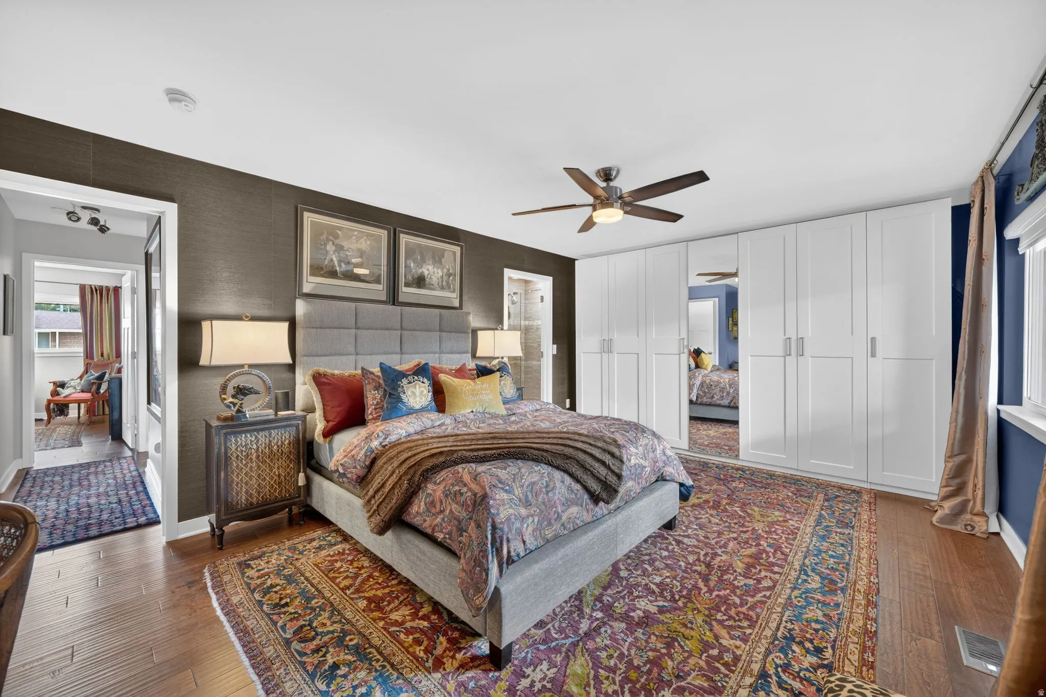 Spacious room featuring wood-finish flooring, a contemporary ceiling fan, and extensive built-in white cabinetry with mirrored accents
