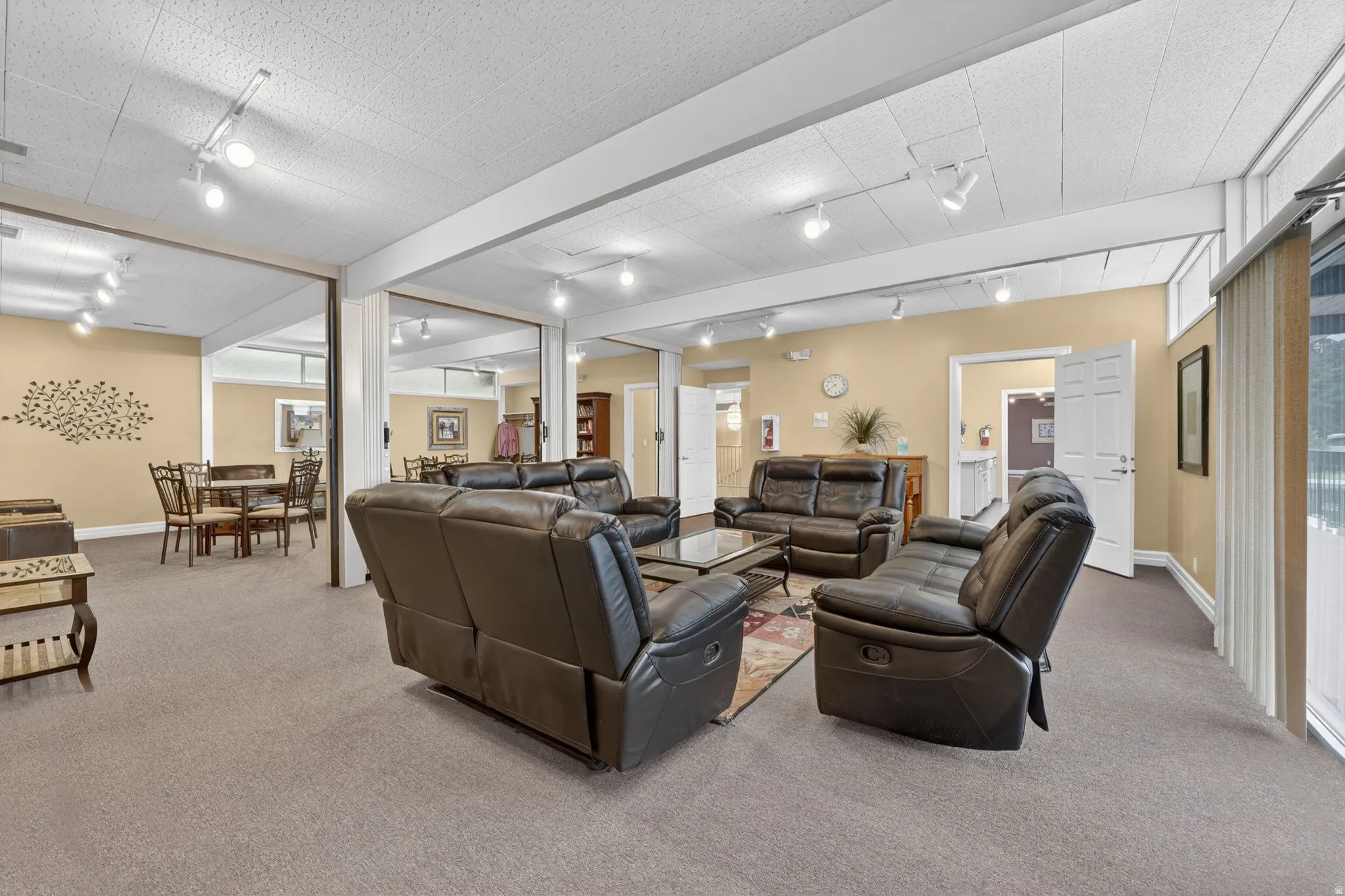 Club house expansive gathering/ hosting area featuring neutral carpeting and track lighting