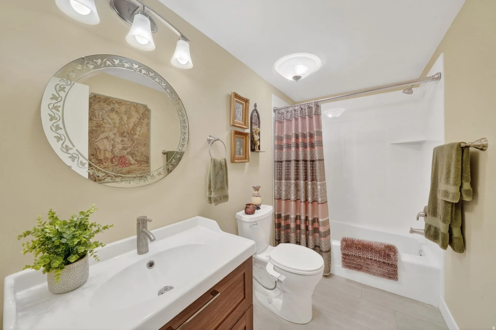 Bathroom featuring a wood-finish vanity with an integrated white sink, a decorative oval mirror, and a full bathtub/ walk-in shower