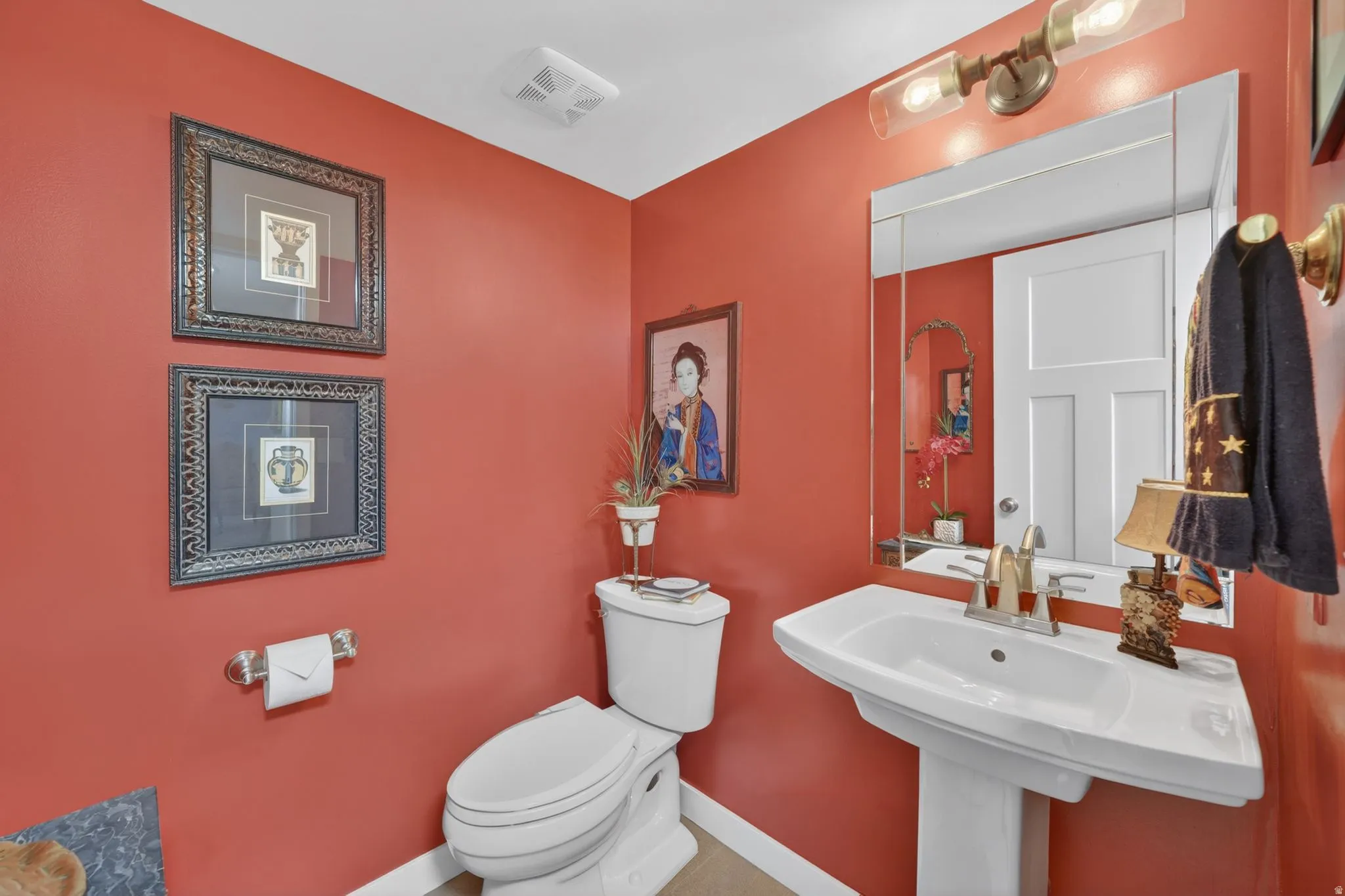 Pedestal sink with chrome faucet, a rectangular mirror, and a two-bulb vanity light fixture