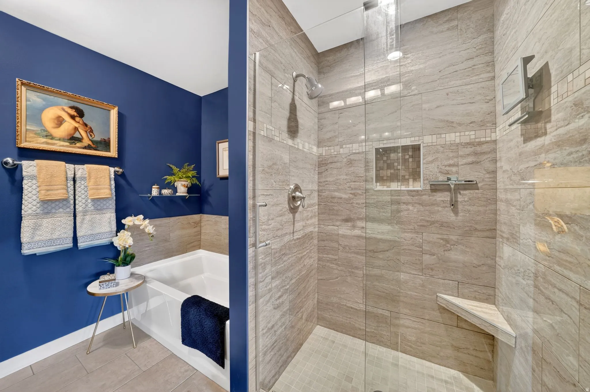 Spacious shower enclosure with glass surround, tiled walls, corner bench, and recessed niche