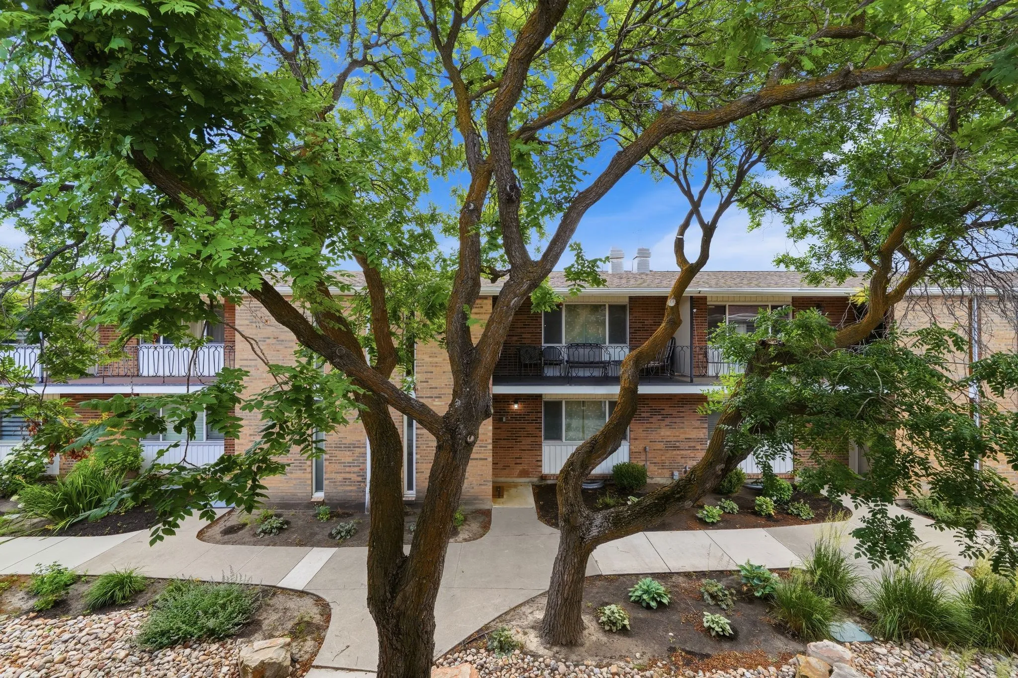 Brick facade building featuring multiple private balconies, ground-level patios, and mature trees