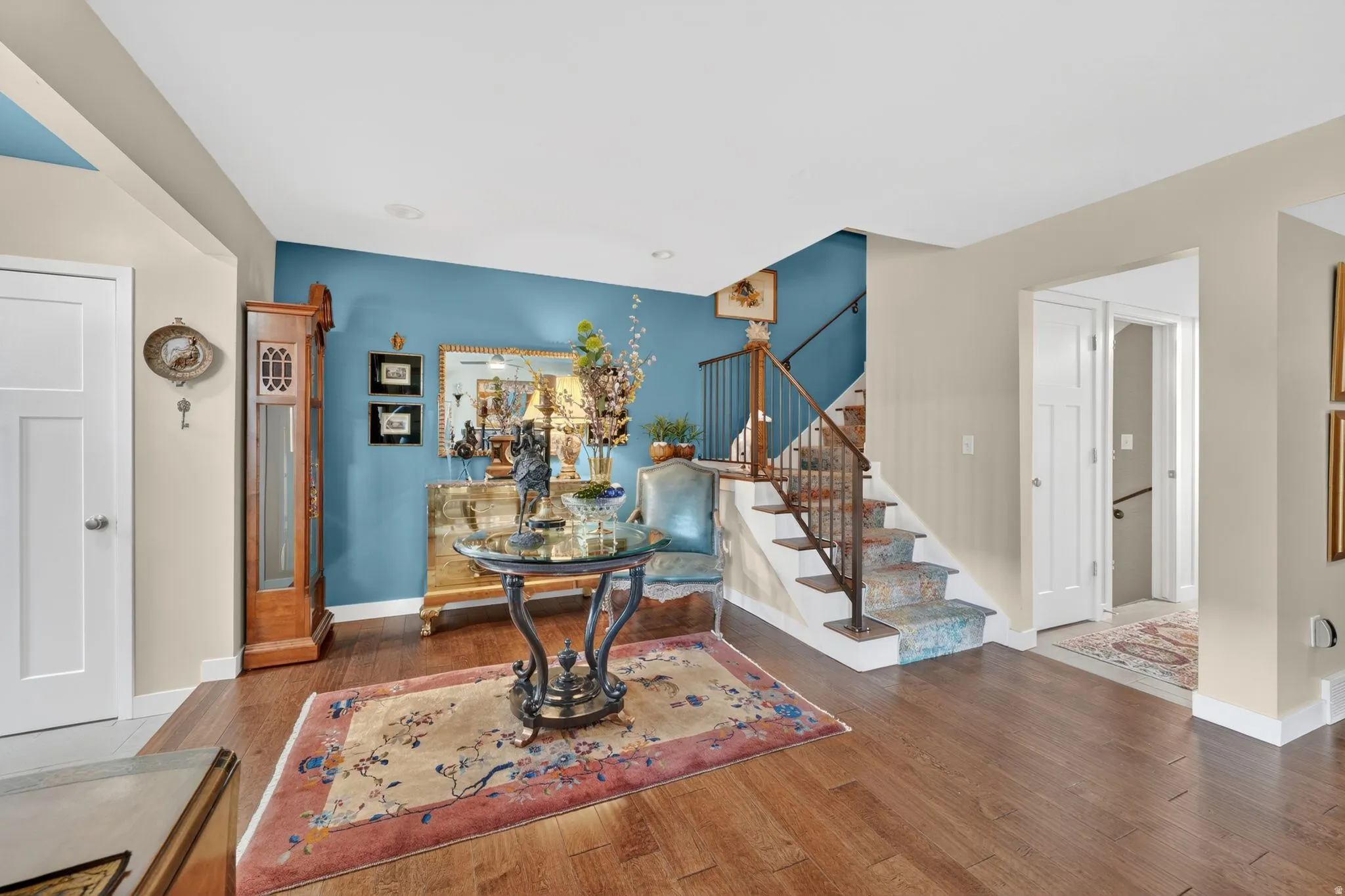 Welcoming entryway featuring engineered hardwood flooring, a vibrant accent wall, white trim, and a staircase with patterned risers