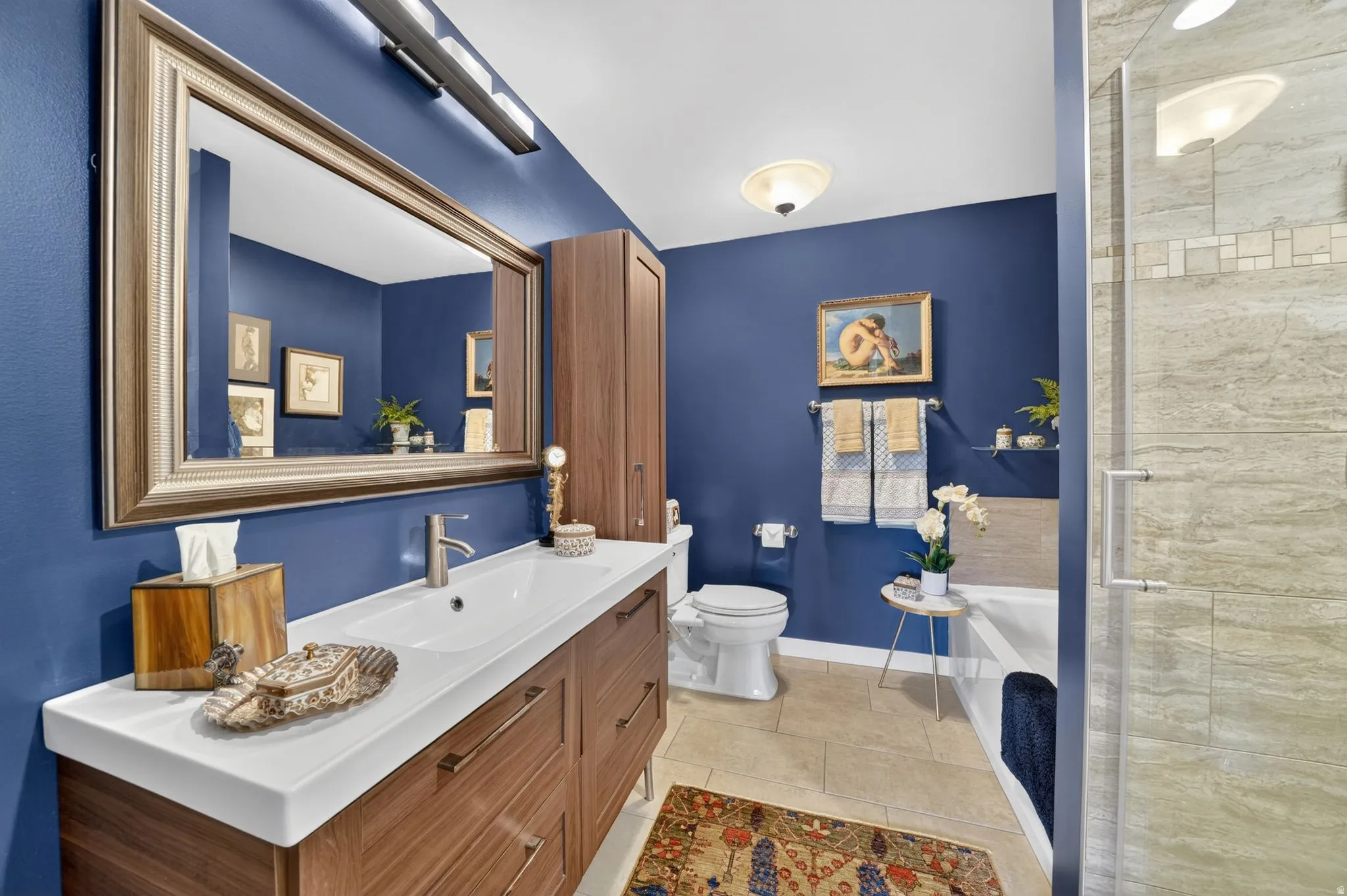 Primary bathroom featuring a long wood-finish vanity with an integrated sink, a large framed mirror, and a built-in storage cabinet