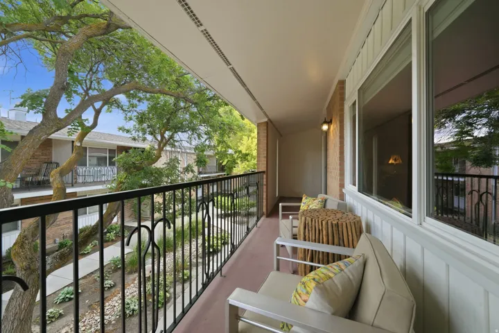 Spacious covered balcony featuring a black wrought-iron railing, white trim, and an exterior wall sconce