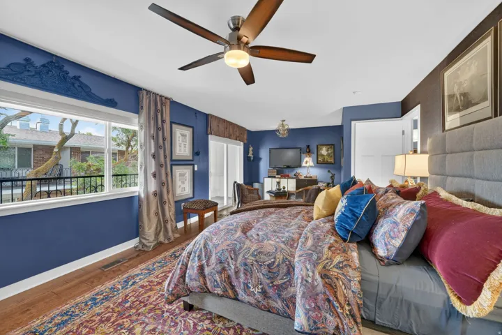 Spacious primary suite featuring engineered hardwood flooring, a contemporary ceiling fan, a wide window, and a walkout to the private deck