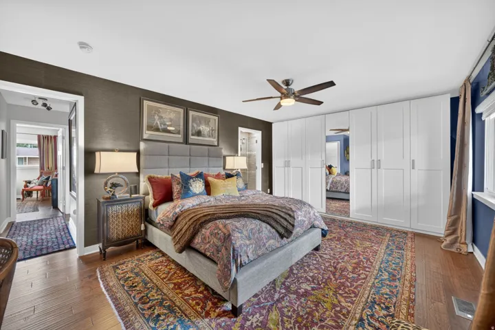 Spacious room featuring wood-finish flooring, a contemporary ceiling fan, and extensive built-in white cabinetry with mirrored accents