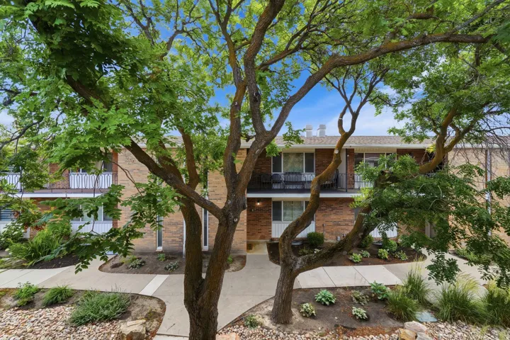 Brick facade building featuring multiple private balconies, ground-level patios, and mature trees