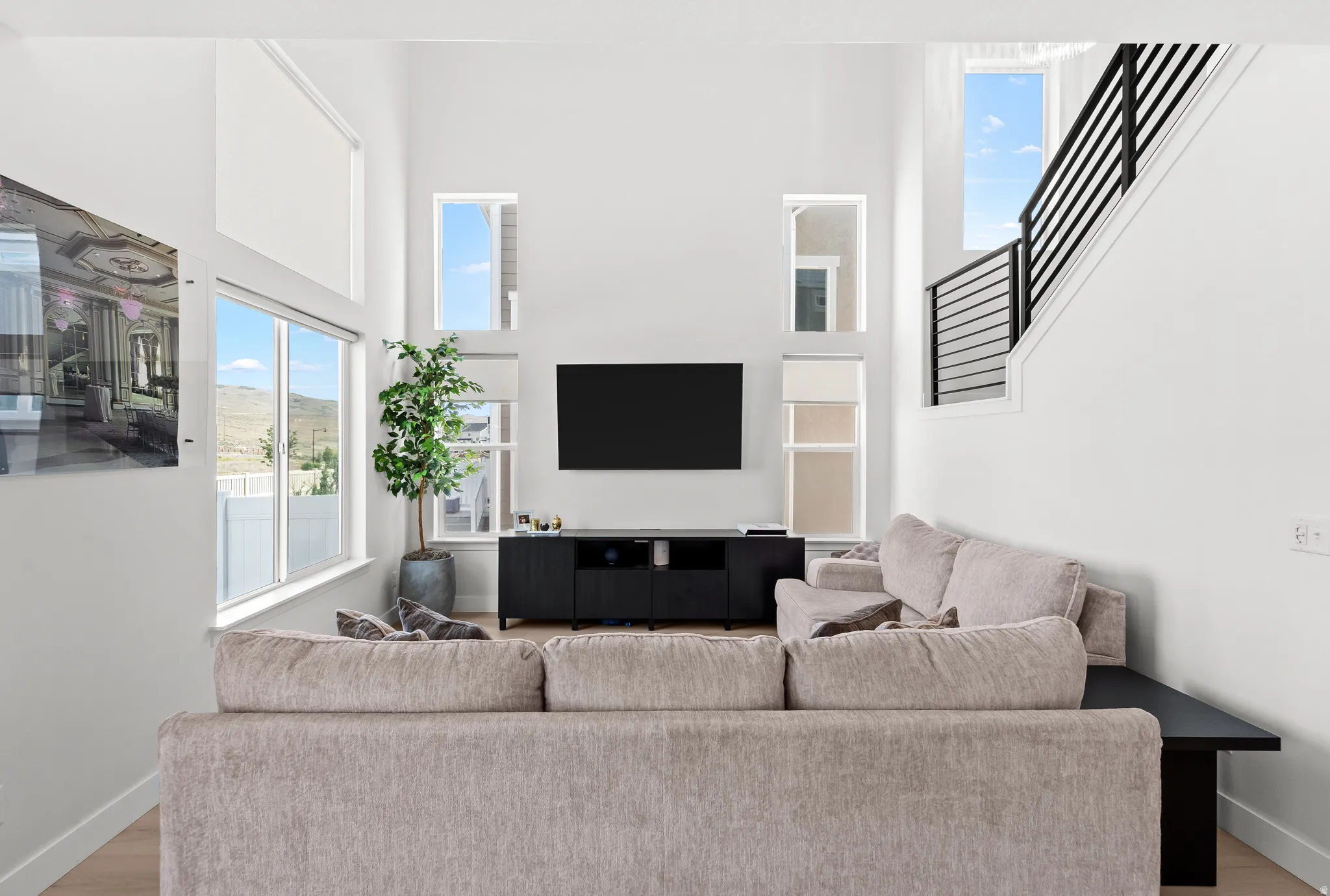 Two-story living area featuring tall ceilings, wood-finish flooring, a wall-mounted media console, and multiple windows