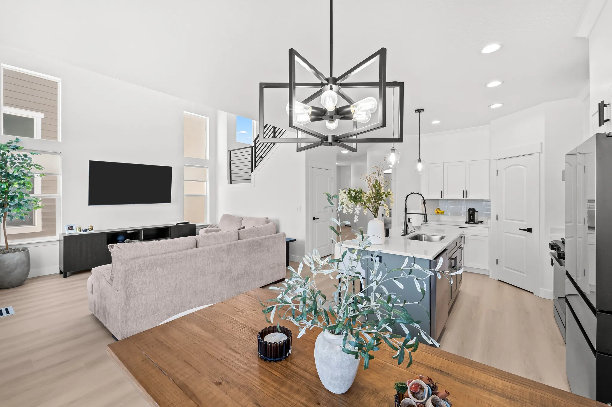 Open-concept living space featuring high ceilings, wood-finish flooring, a modern chandelier, and a kitchen island with a sink and pendant lighting