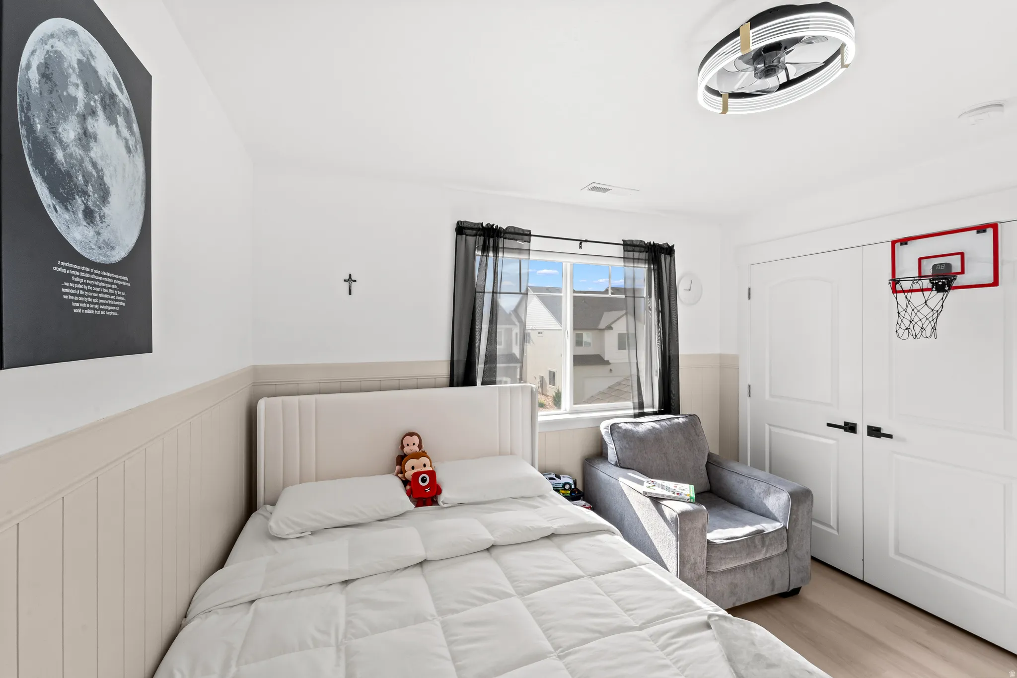 Room featuring vertical paneling, a large window with black sheer curtains, and a ceiling fan with integrated lighting