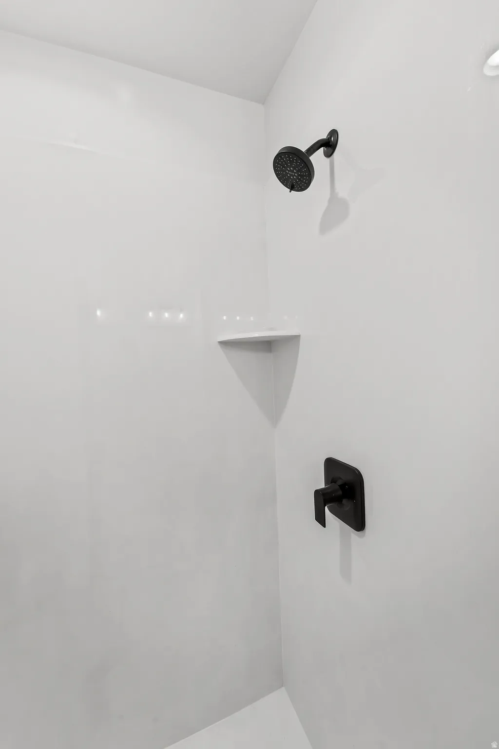 Shower enclosure featuring white paneling, a matte black showerhead, a built-in corner shelf, and a matte black single-handle control