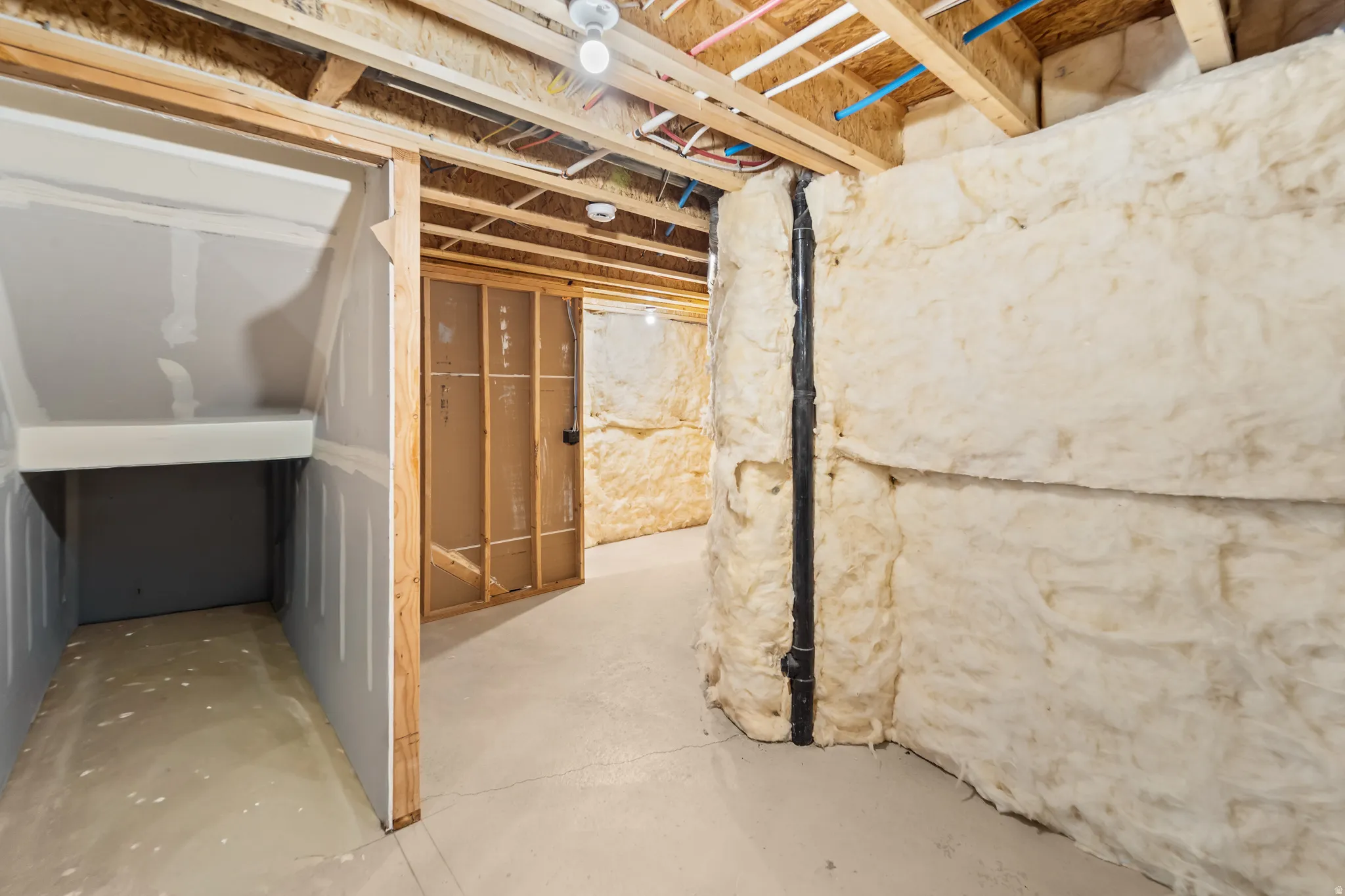 Unfinished basement offering exposed ceiling joists, concrete flooring, insulated walls, and visible plumbing lines