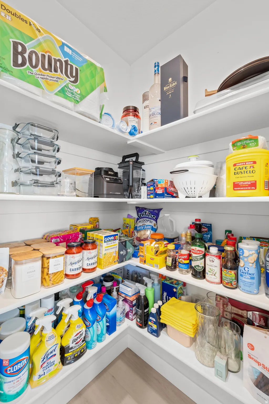 Spacious corner pantry featuring white built-in shelving, ample storage capacity, and wood-finish flooring