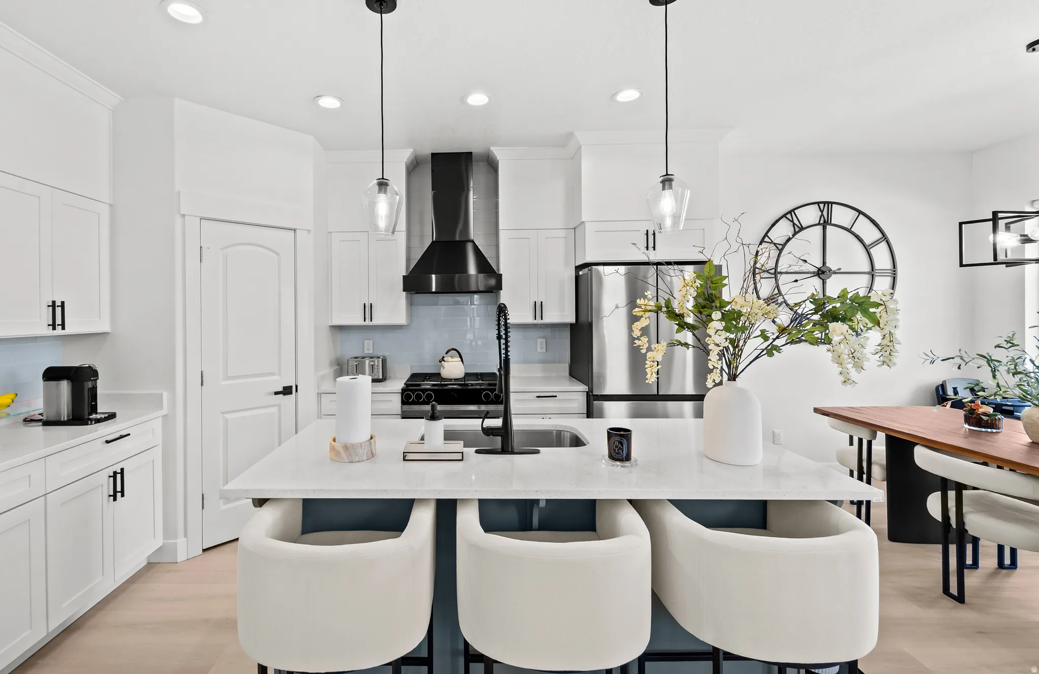 Modern kitchen featuring a central island with white countertop, white cabinetry with matte black hardware, stainless steel appliances, a light blue subway tile backsplash, and wood-finish flooring