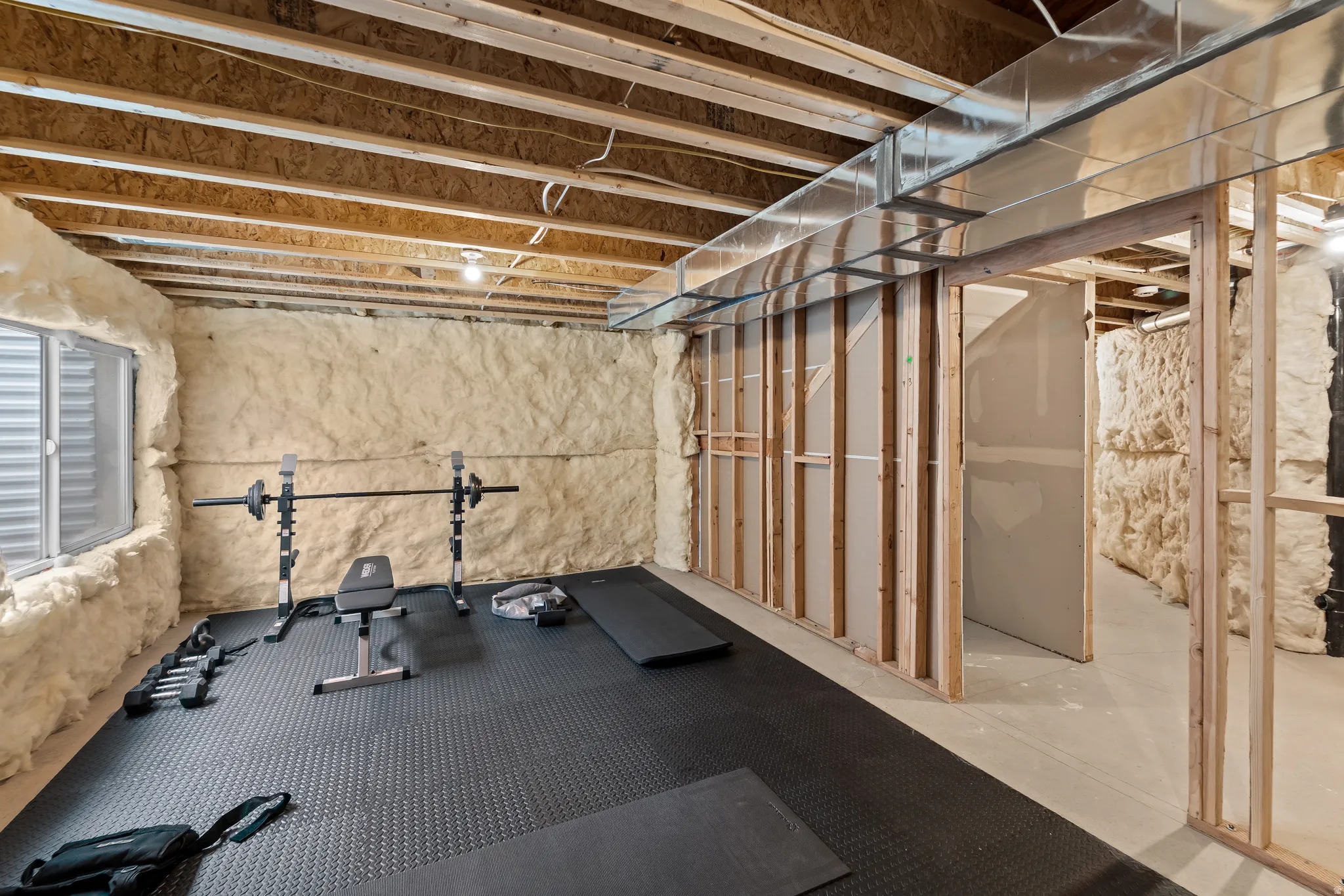 Unfinished basement space featuring exposed wood joists, spray foam insulation on exterior walls, a window well, and wood framing for potential interior rooms
