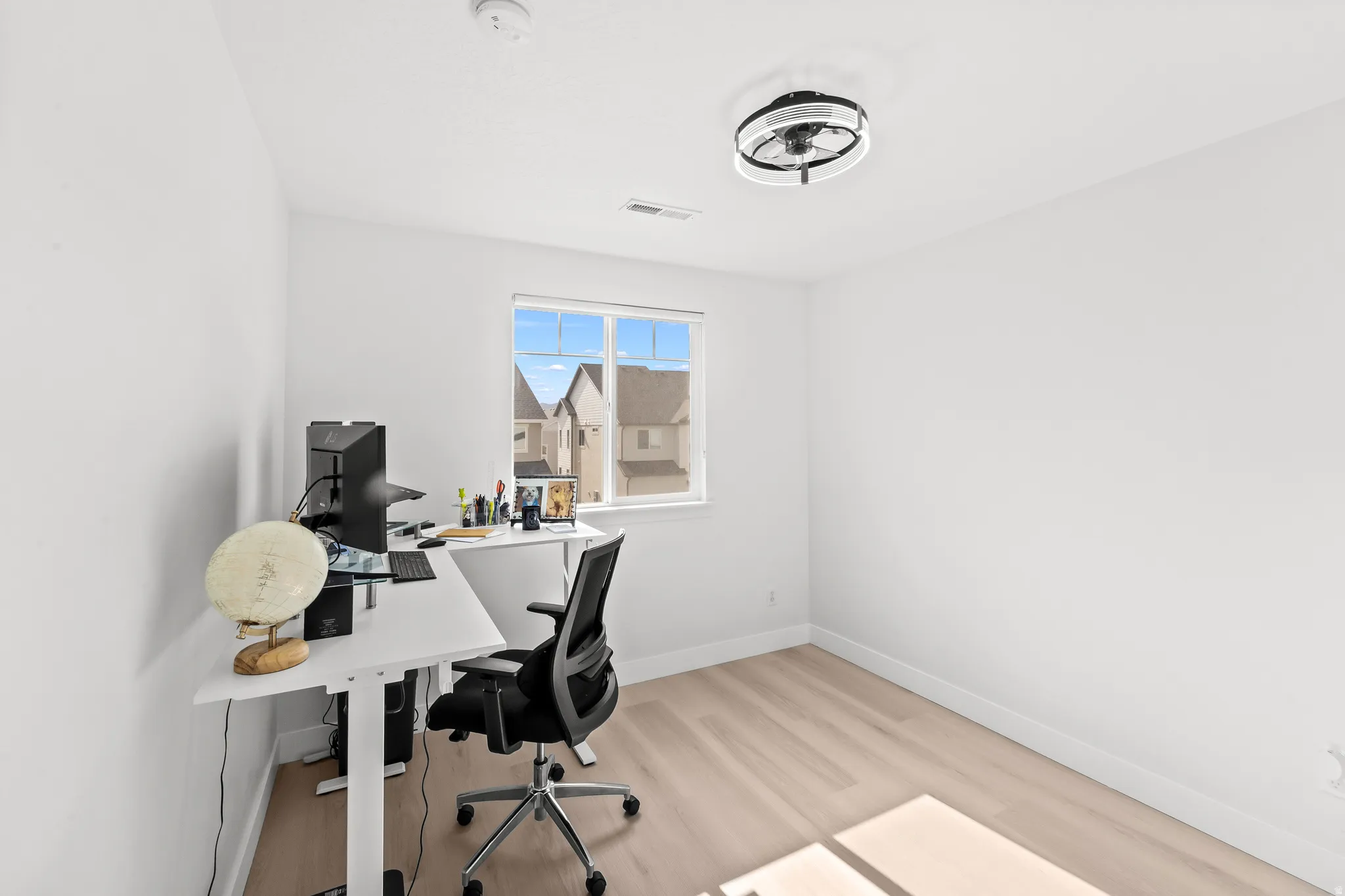 Bright room with light wood-finish flooring, white walls, and a contemporary ceiling fan