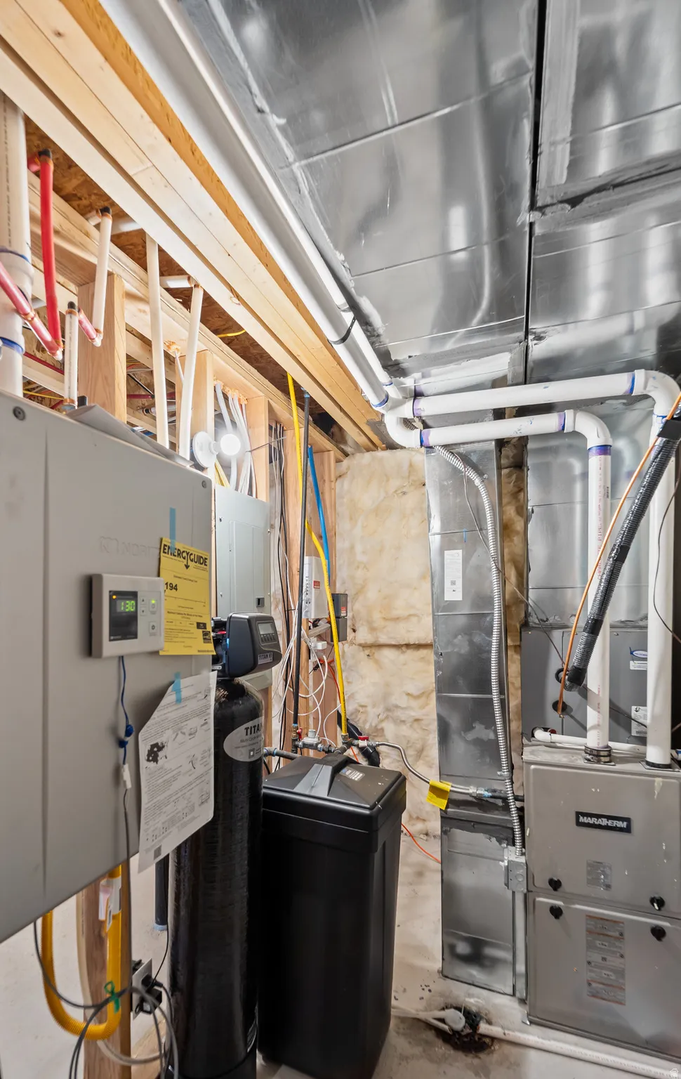 Utility area featuring exposed wood framing, multiple HVAC units, a water softener system, and extensive plumbing and ductwork