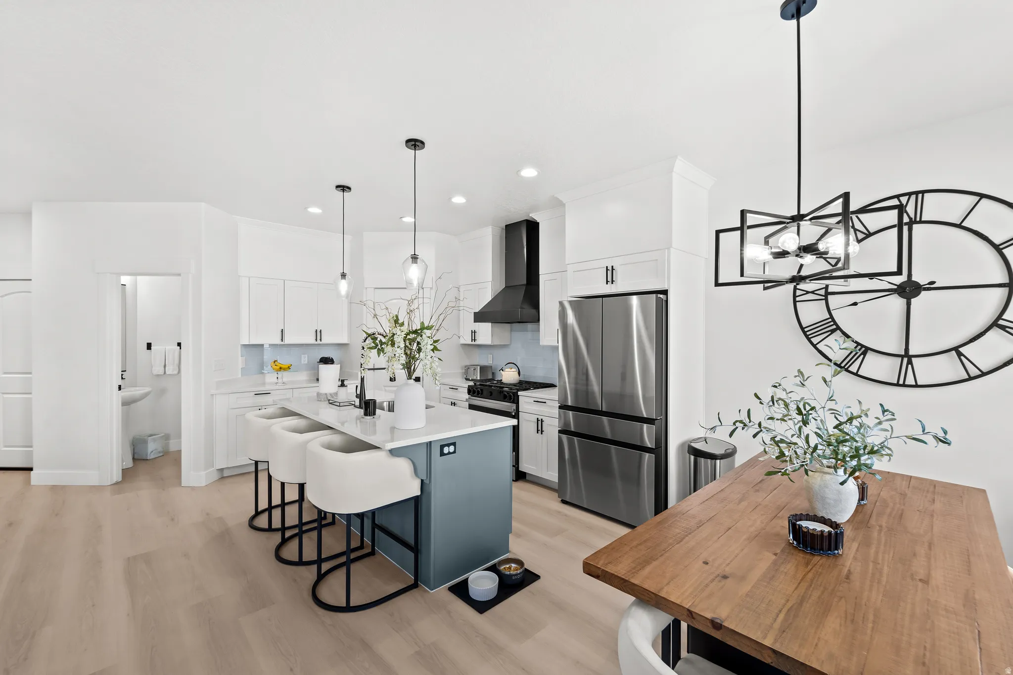 Open-concept kitchen featuring an oversized island with seating, pendant lighting, stainless steel appliances, white cabinetry, and wood-finish flooring