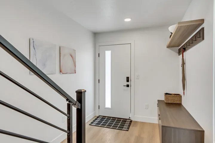 Entryway featuring light wood-finish flooring, a modern white door with a vertical frosted glass insert, and a black metal stair railing