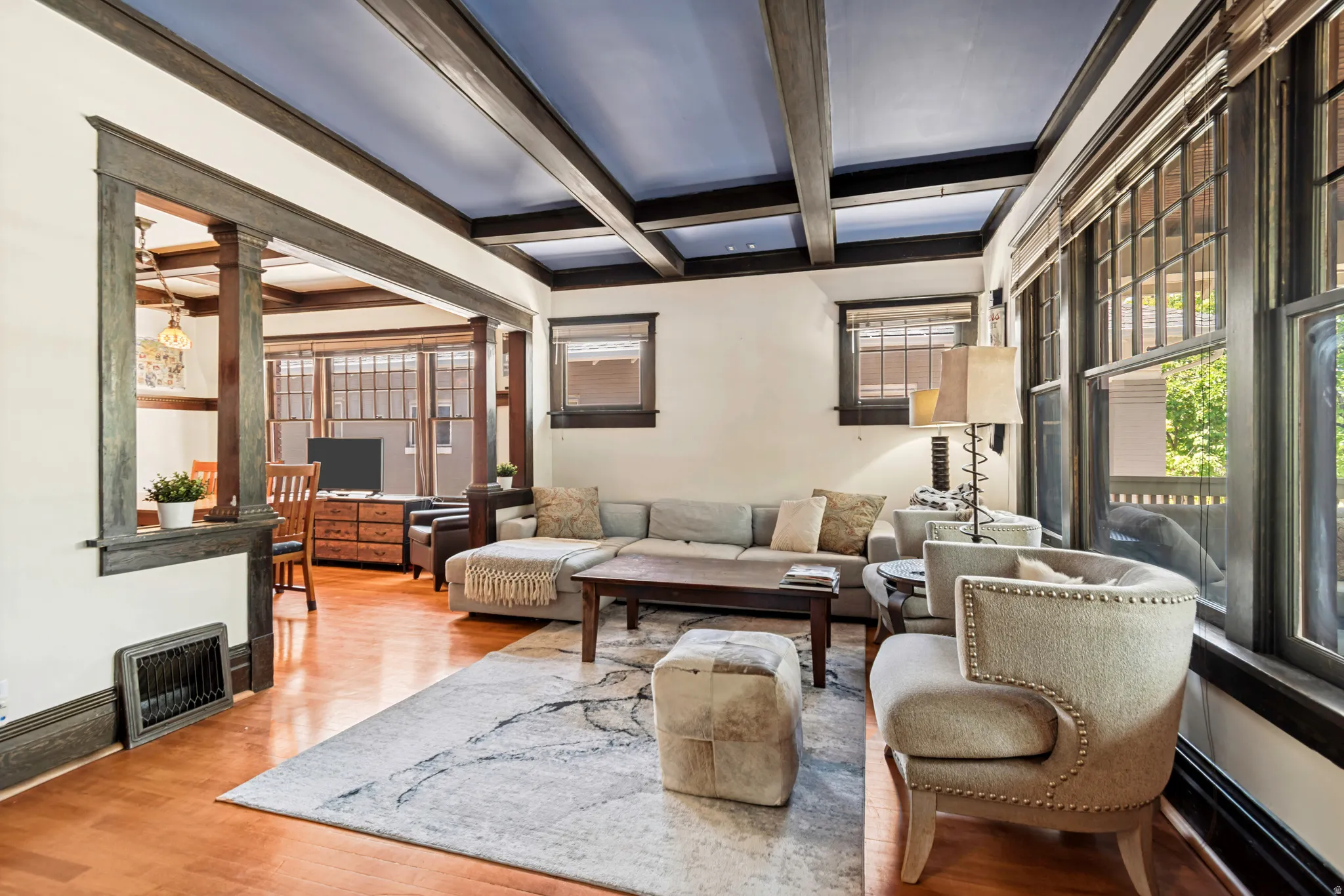 Living area featuring wood-finish flooring, a coffered ceiling with dark beams, and prominent windows
