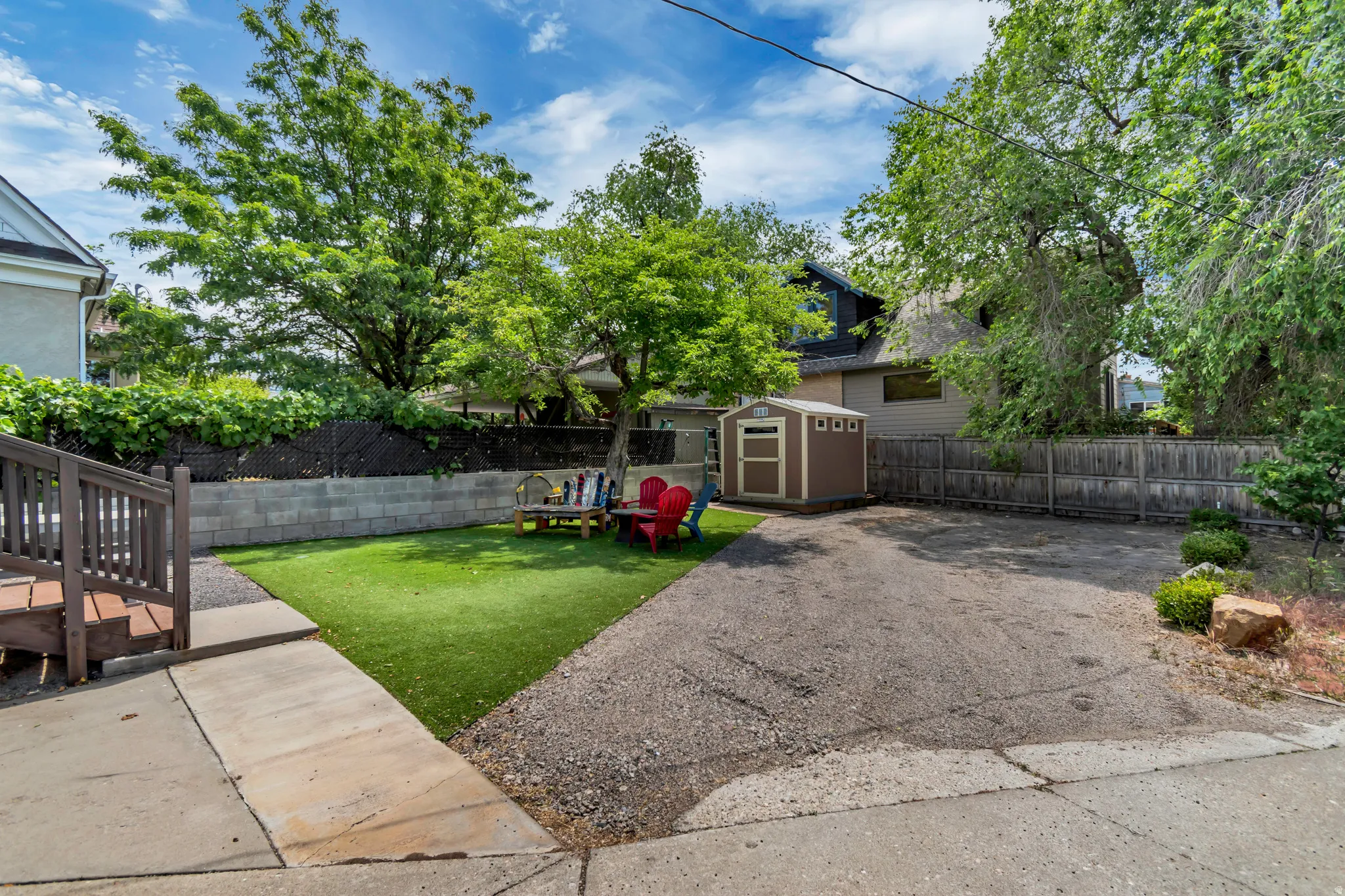 Expansive rear yard featuring a paved drive, artificial turf lawn, and mature trees